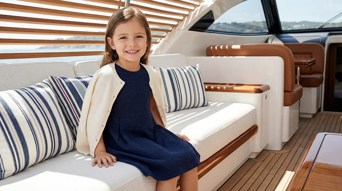 Девочка в синем жаккардовом платье Fendi Kids и кремовом кашемировом кардигане на борту роскошной яхты, тренды итальянской детской моды 2026 в стиле тихой роскоши.